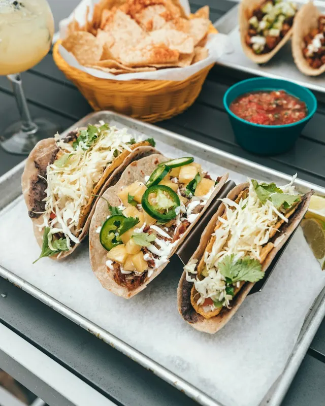 Three soft tacos topped with fresh vegetables and salsa